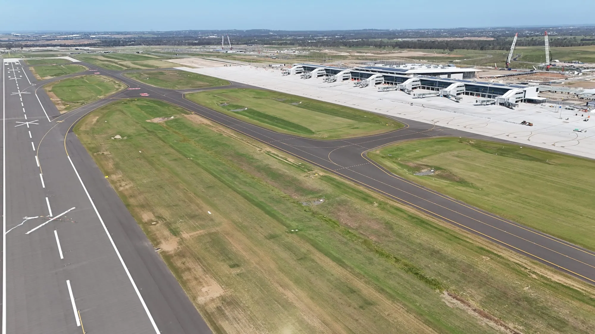 The airport’s single runway seen from the air, its surface marked with white crosses, with a parallel taxiway alongside and the terminal building beyond.